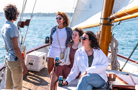 A group of three girls talking to a crew member on the decks of schooner Madeleine for a Newport Morning Mimosa Cruise