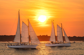 Two Schooners sailing at Sunset in Newport RI with the sun casting a golden glow in the sky