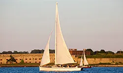 Newport_Private-Boat-Charters_Sloop-Eleanor the sloop eleanor sailing down the river, with buildings behind it out in the distance